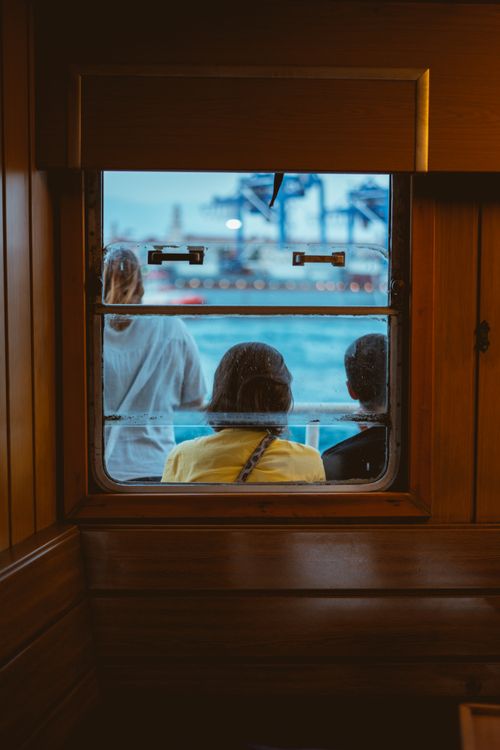 Free A group of three people sitting and gazing at the harbor view through a ship window. Stock Photo