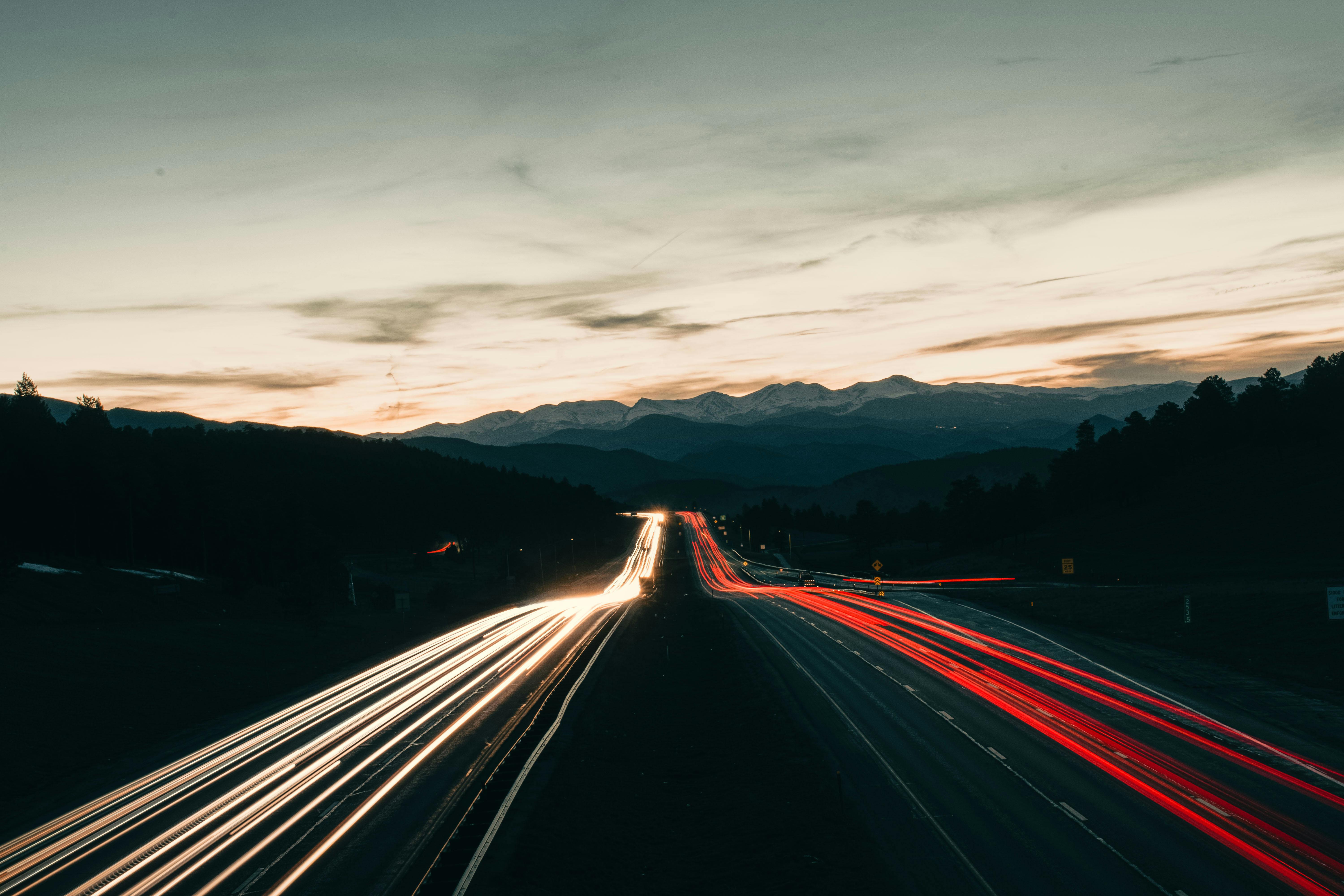 Captivating long exposure of highway light trails under Colorado's twilight sky, featuring distant mountains.