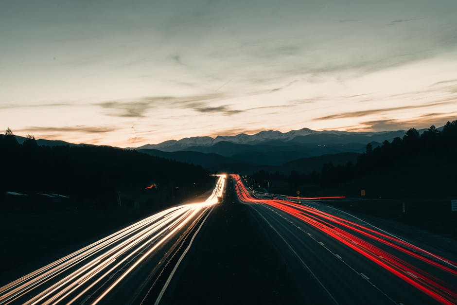 Captivating long exposure of highway light trails under Colorado's twilight sky, featuring distant mountains.