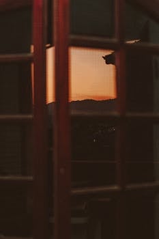 A serene sunset view through a balcony door with silhouetted details.