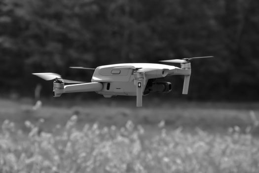 Monochrome image of a drone hovering outdoors over grassy field.