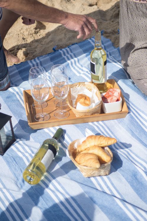 Free Relaxing beach picnic scene with wine, pastries, and a wooden tray on a striped blanket in Portugal. Stock Photo