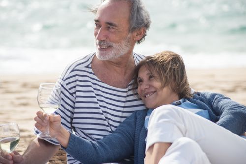 Free Senior couple smiling and enjoying white wine on a sunny beach in Portugal. Stock Photo