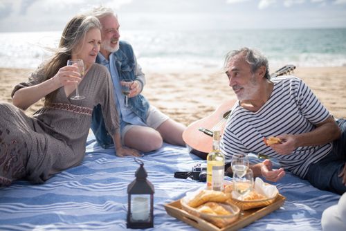 Free Three seniors bond over wine and snacks during a beach picnic, enjoying a sunny day in Portugal. Stock Photo