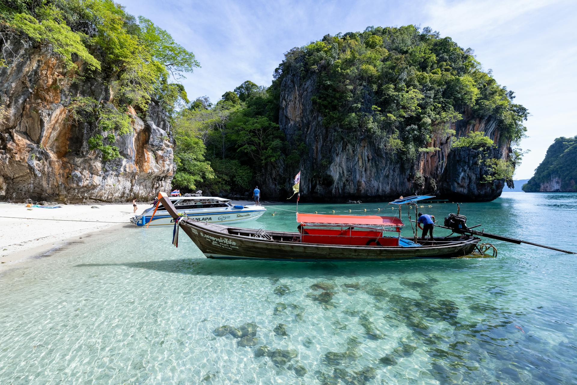 Peaceful Thai beach with clear waters, longtail boat, and limestone cliffs. A perfect tropical escape.