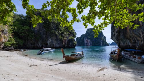 Free Tranquil Thai beach with moored boats and stunning cliffs, perfect for travel lovers. Stock Photo