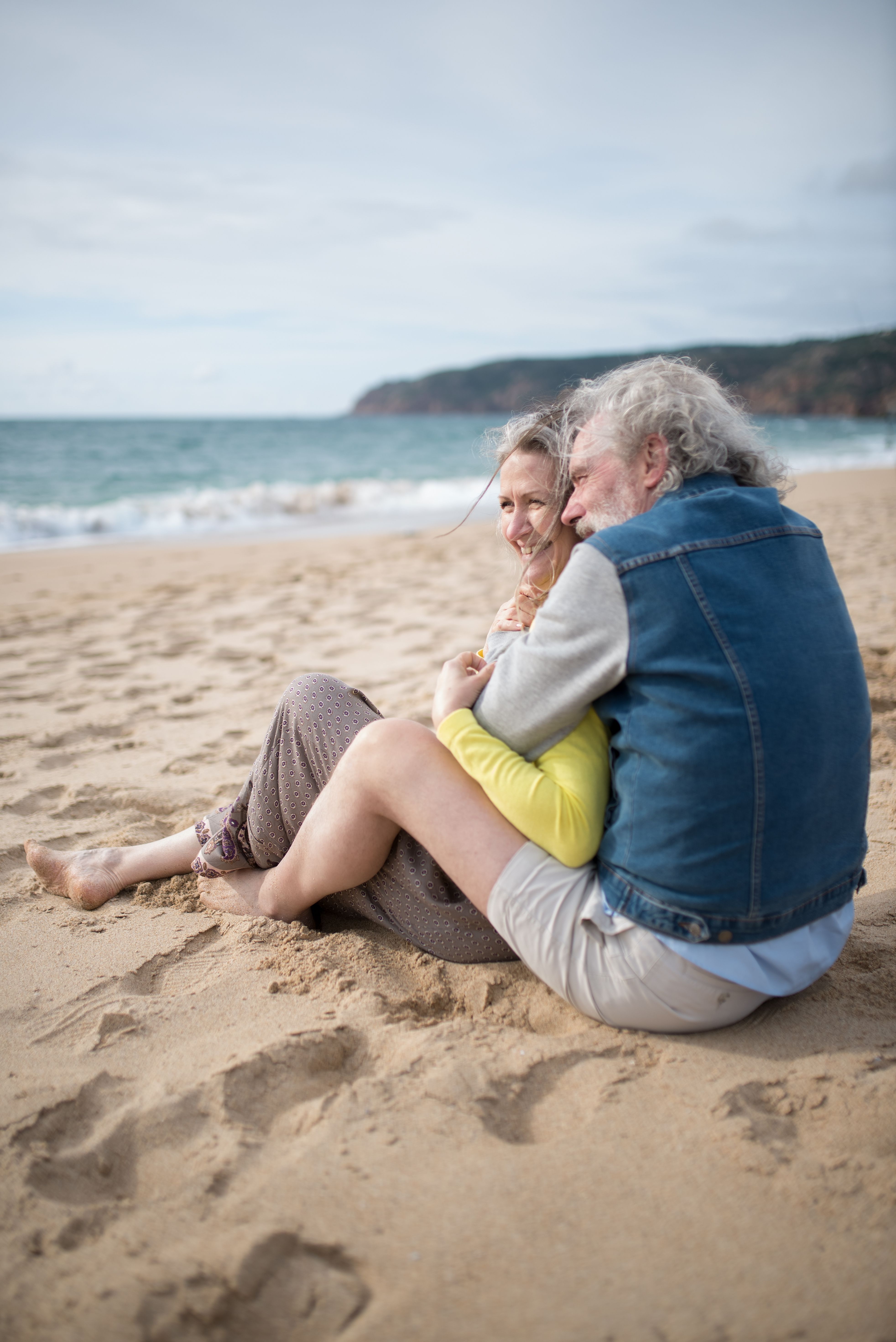 An elderly couple embracing on a sunny Portuguese beach, captured in a warm, romantic setting.