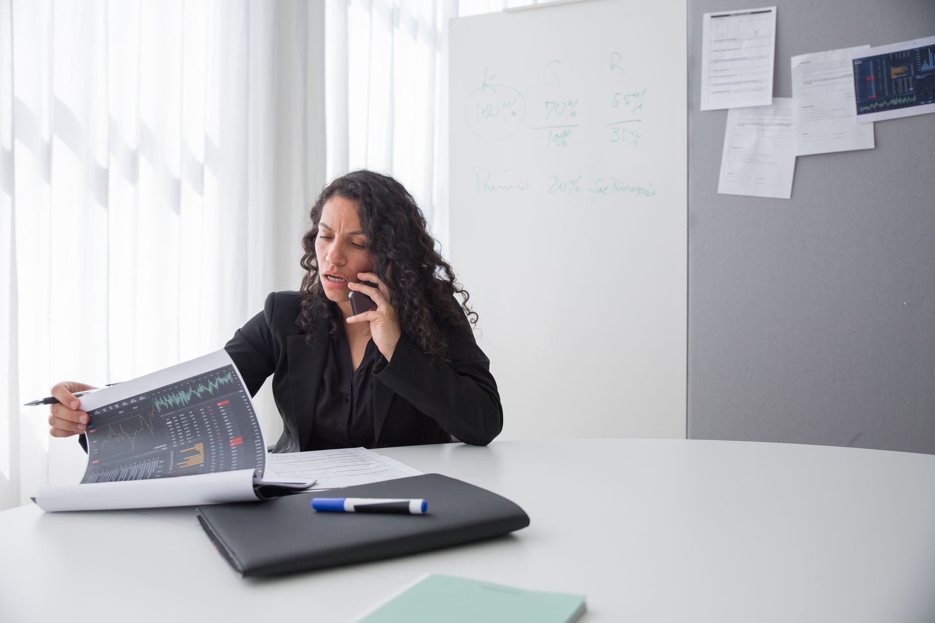 Focused businesswoman reviewing data charts during a phone call in a modern office setting.
