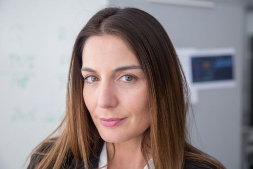 Free Close-up portrait of a confident woman with long hair indoors, expressing warmth and professionalism. Stock Photo