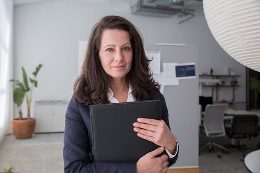 Confident businesswoman in blazer holding binder in modern office.