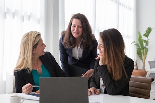 Three professional women engaged in a collaborative business discussion in a modern office setting.