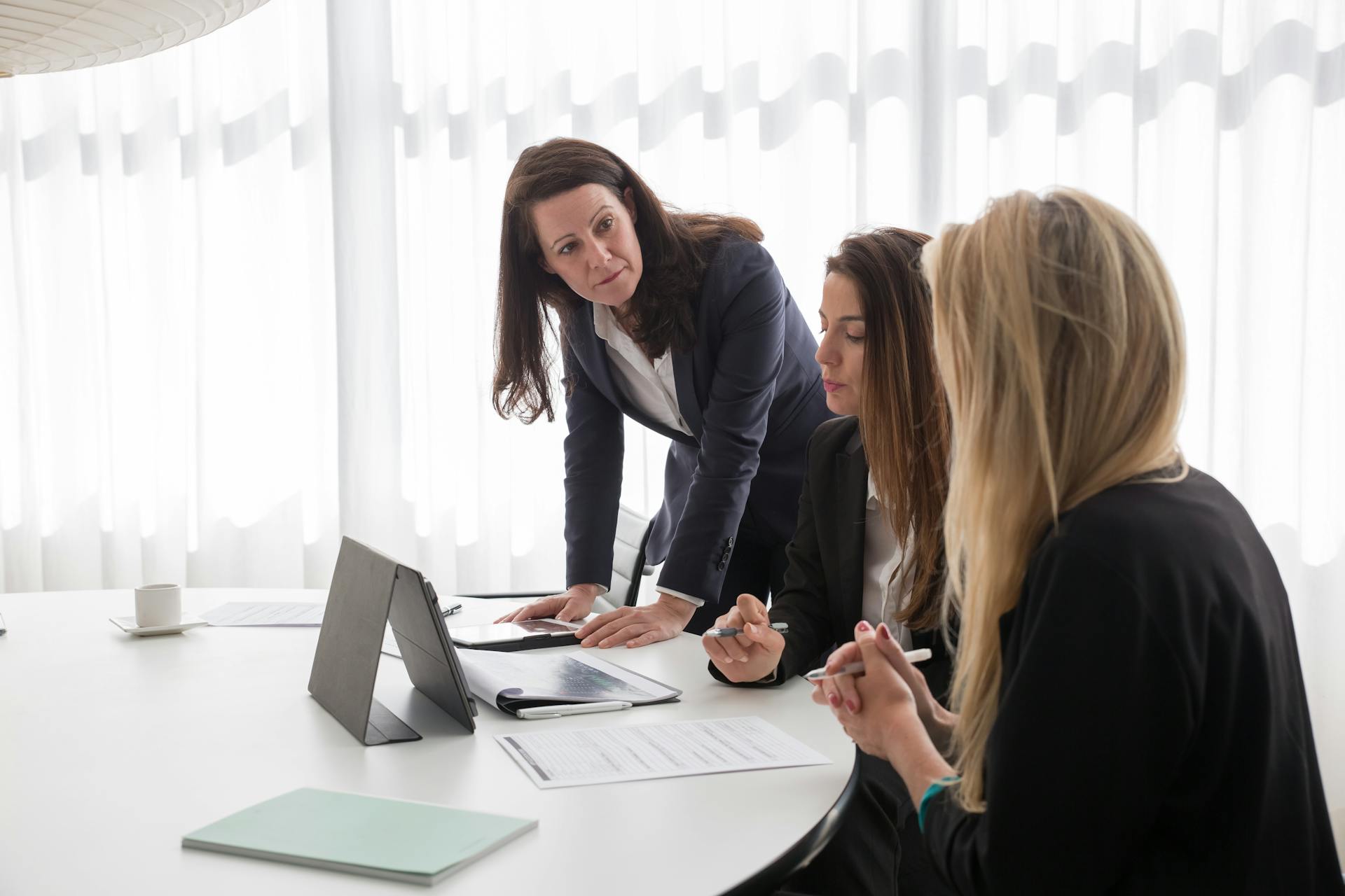 Three businesswomen engaged in a meeting with documents and a tablet in a modern office.