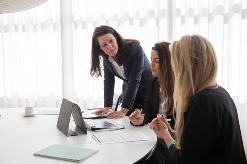 Free Three businesswomen engaged in a meeting with documents and a tablet in a modern office. Stock Photo