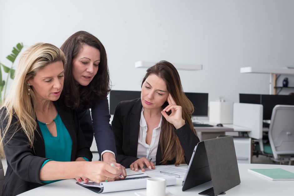 Tres mujeres de negocios colaboran en documentos en un ambiente de oficina moderno.