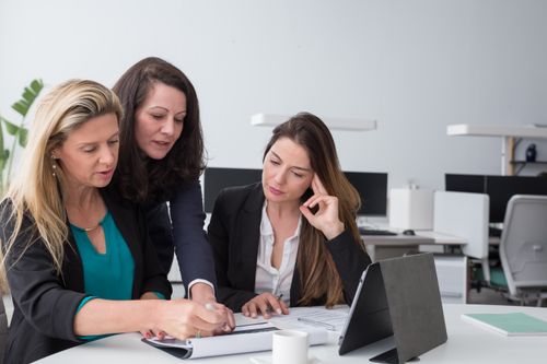 Free Three businesswomen collaborate on documents in a modern office setting. Stock Photo