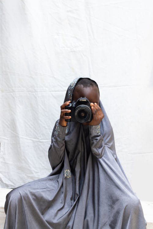 Photo of a Kid in Traditional Clothes Holding a Black Camera