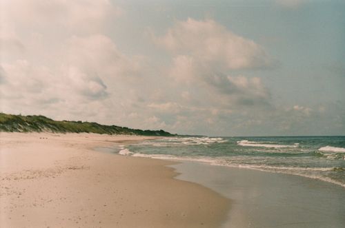 Free Serene sandy beach with gentle waves and a cloudy sky, perfect for relaxation and nature lovers. Stock Photo