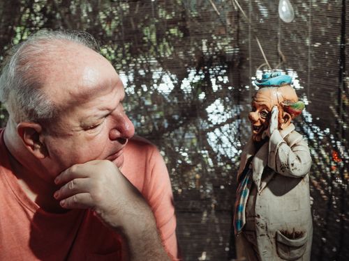 Free An elderly man in contemplation gazes at a quirky figurine indoors in natural light. Stock Photo