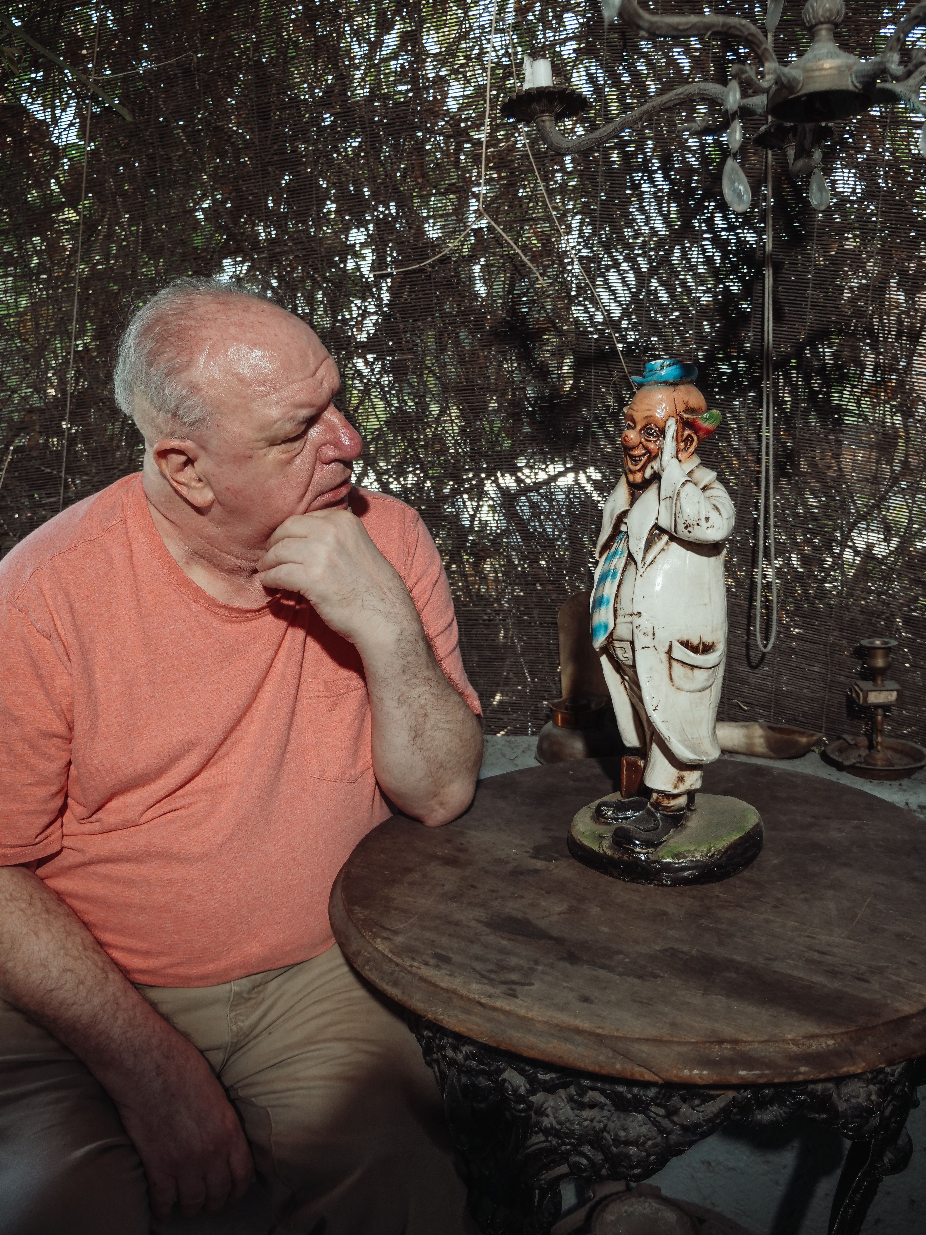 Senior man thoughtfully observing a clown sculpture on a table indoors.