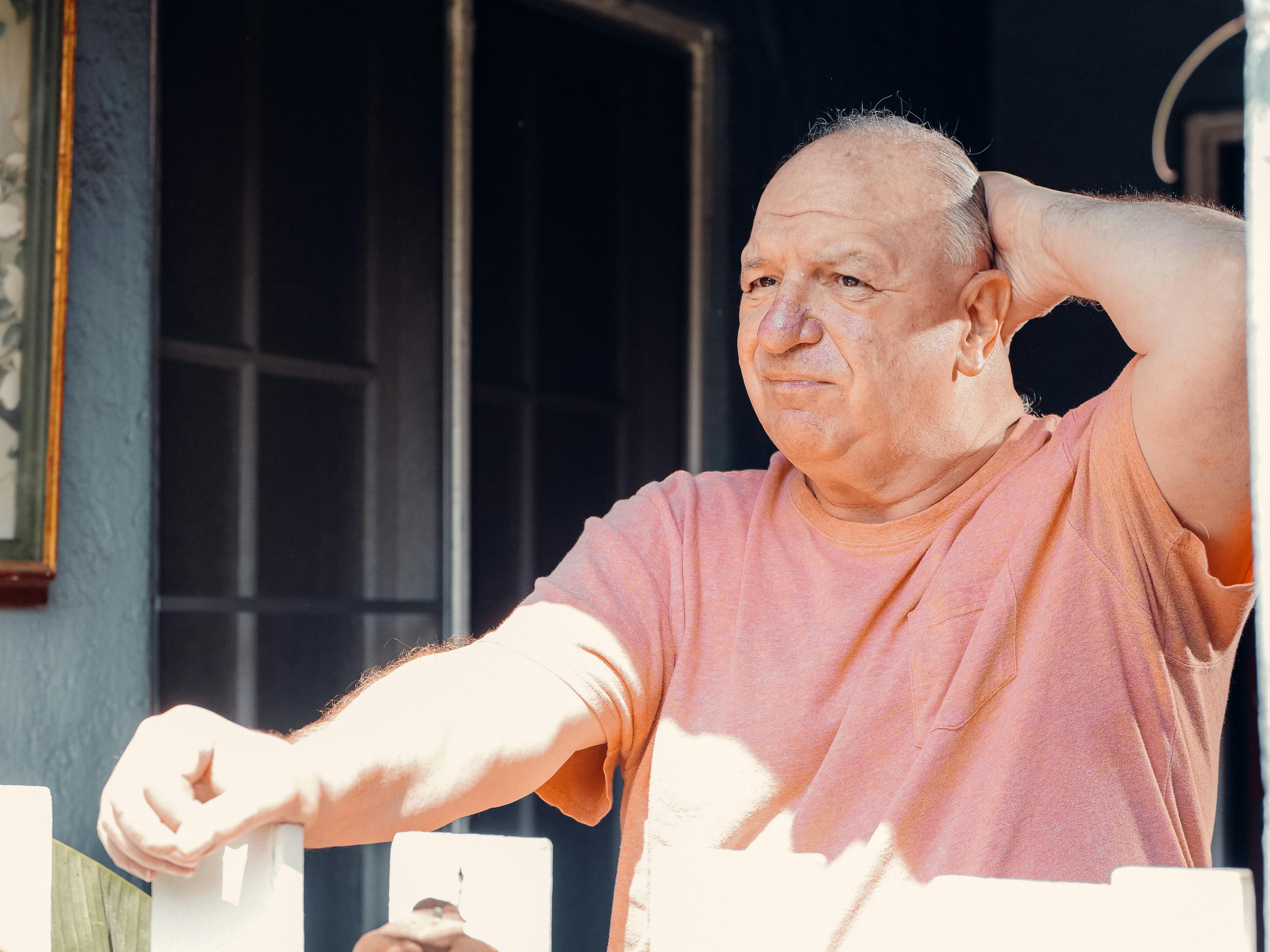 an elderly man looking outside with his hand on his head