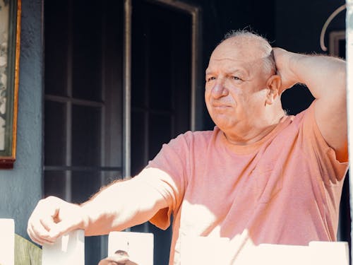 An Elderly Man Looking Outside with His Hand on His Head
