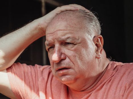 Close-up of a senior adult man looking troubled with hand on head, expressing stress.