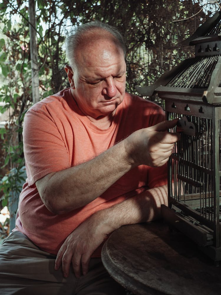 An Elderly Man Holding A Door Of A Birdcage