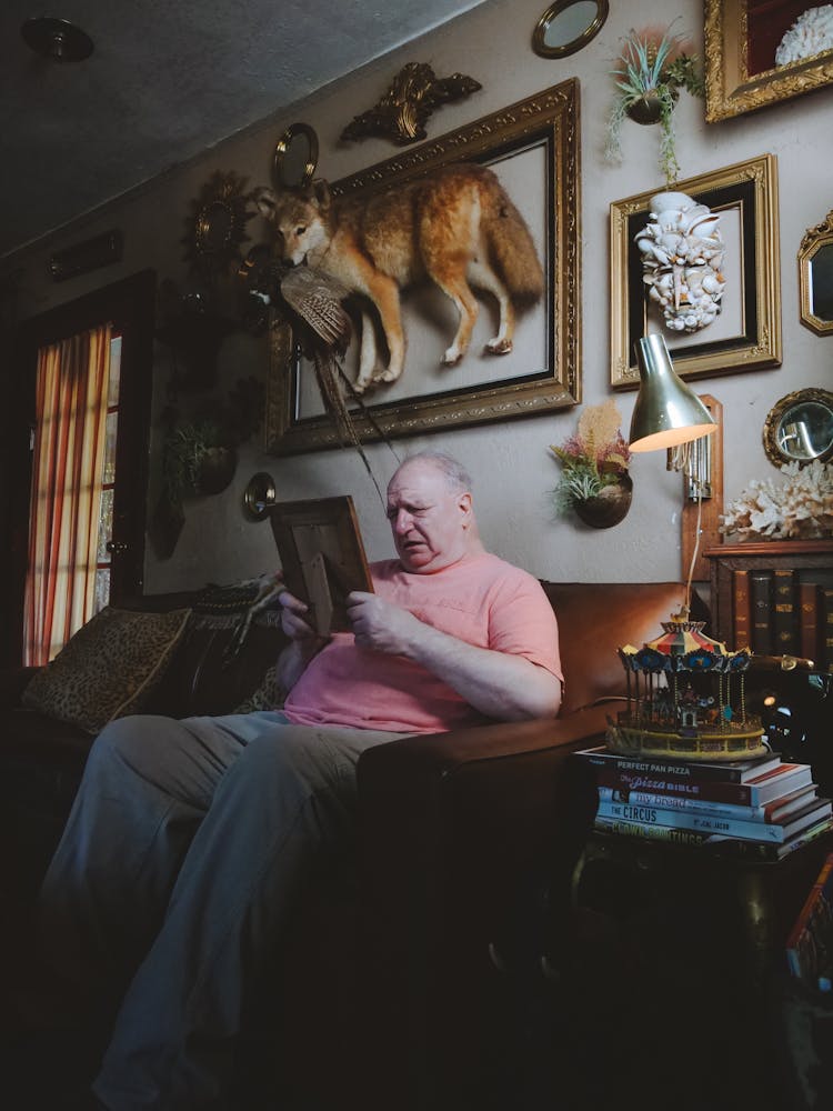 An Elderly Man Sitting On The Couch Crying While Looking At The Picture Frame