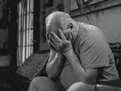 An Elderly Man Sitting on the Couch while Covering His Face