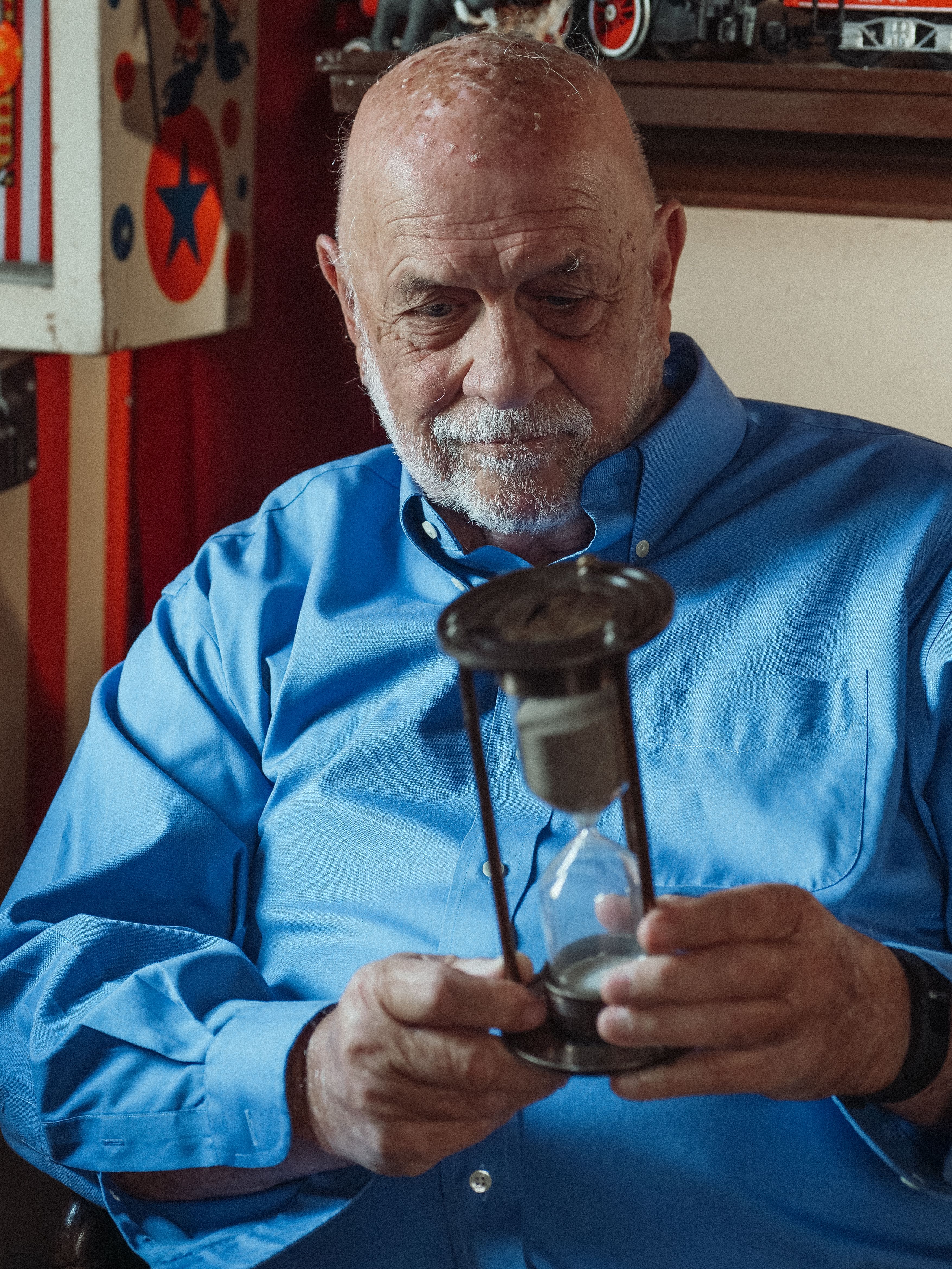 Senior man pondering time while holding an hourglass indoors.