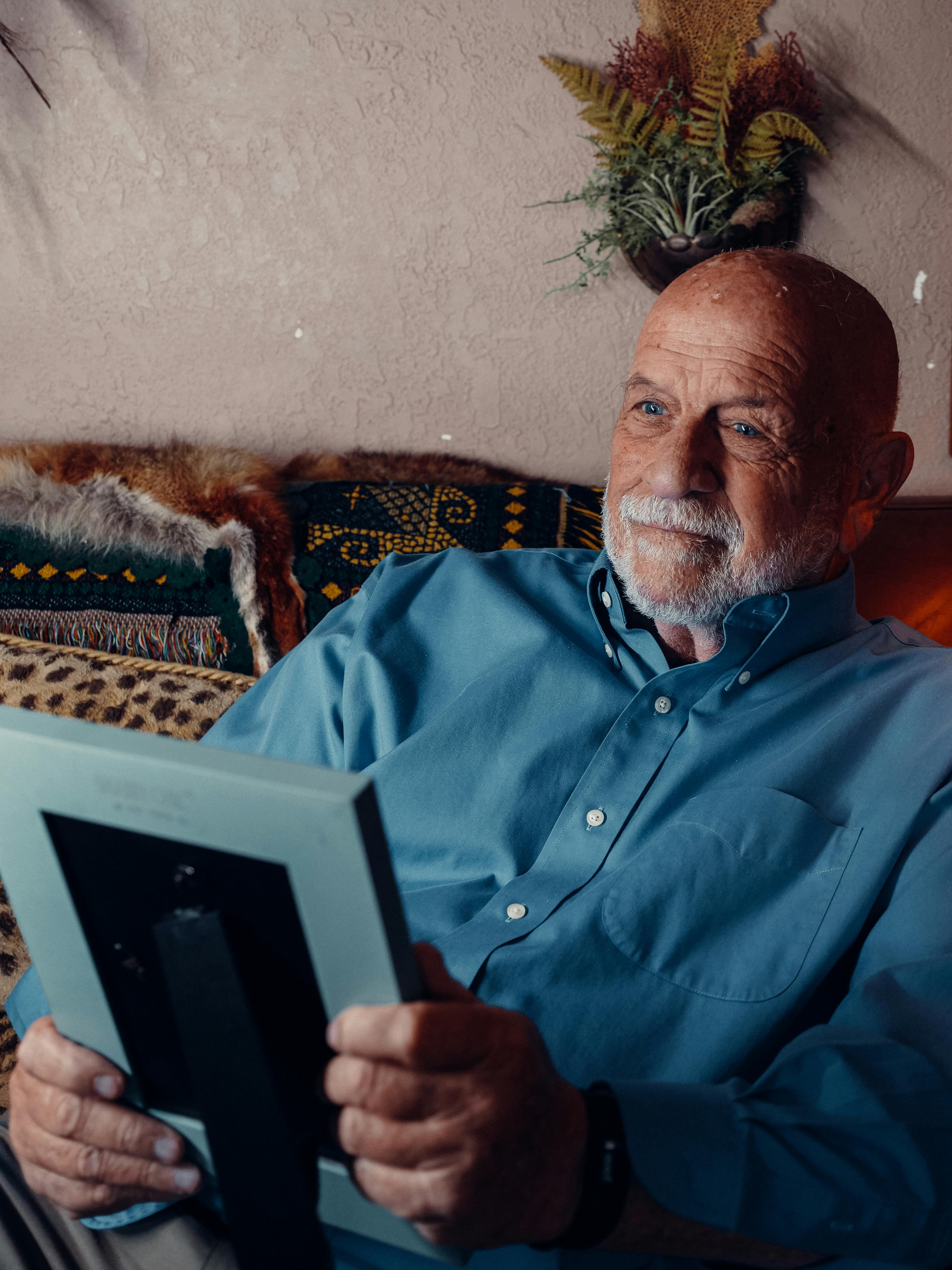 Elderly man with beard smiling while holding a picture frame, reflecting on memories.