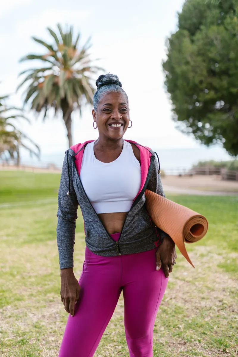 An older woman carrying her yoga mat before a movement session