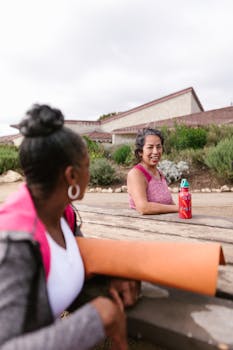 Two women enjoy a friendly conversation during an outdoor yoga session, promoting wellness and togetherness.