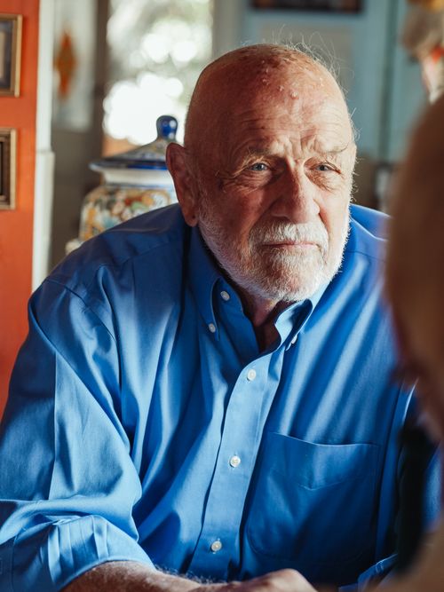 Free Portrait of an elderly man with a beard in a blue shirt, sitting indoors and looking thoughtful. Stock Photo