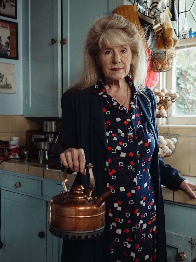 An Elderly Woman Holding A Kettle In The Kitchen