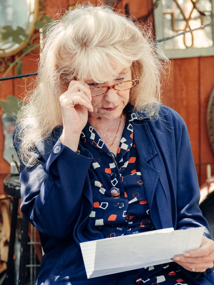 An Elderly Woman Reading A Letter While Holding Her Eyeglasses