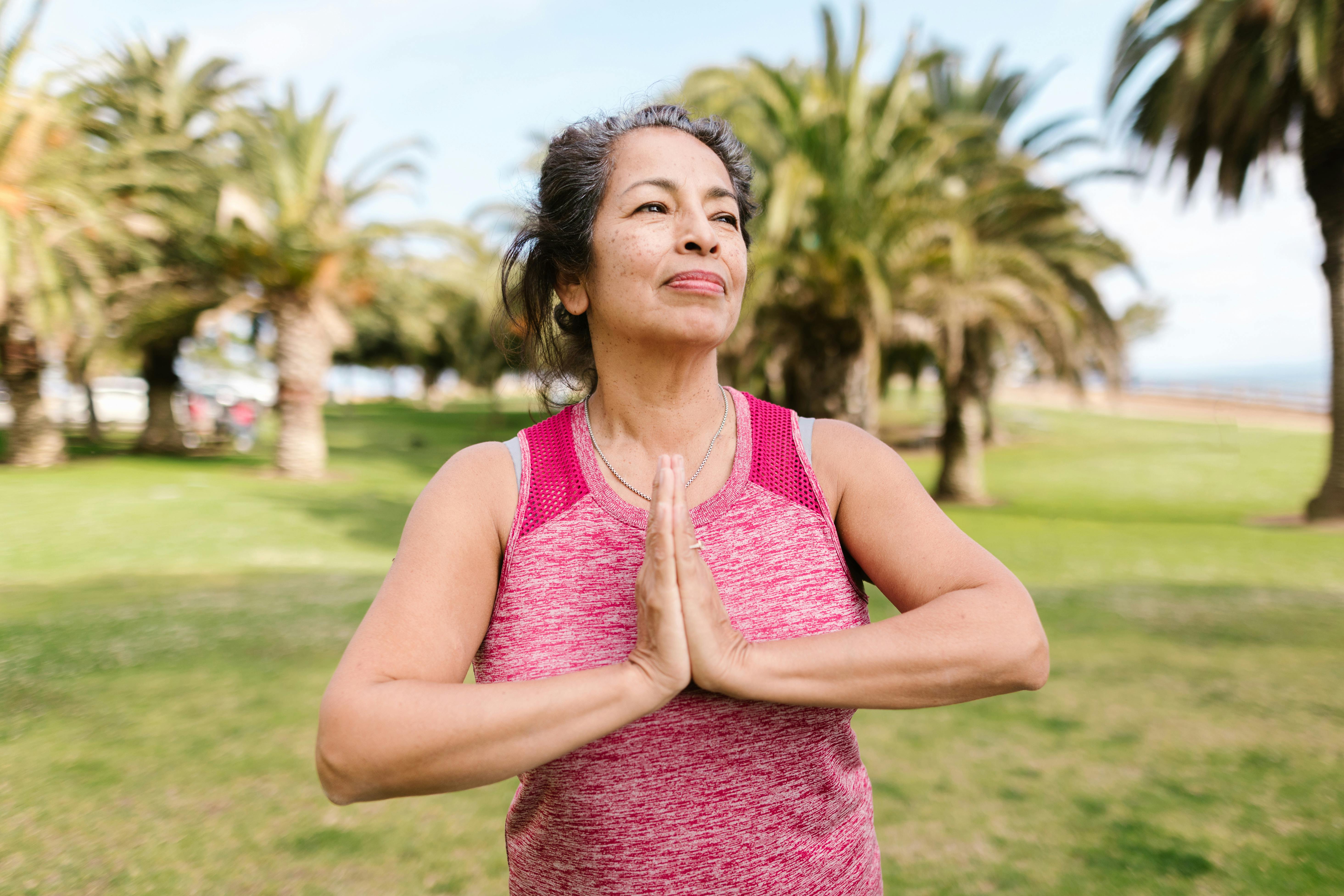 an elderly woman in pink tank top with her hands together