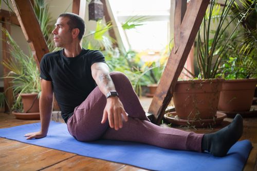 Free A man wearing activewear practices yoga on a mat indoors amid plants. Calm and focused. Stock Photo