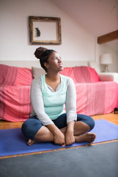 A woman in activewear smiling while sitting cross-legged on a yoga mat indoors, promoting a healthy lifestyle.
