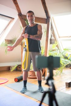 A young man demonstrating exercises with a resistance band indoors, captured in a bright room.