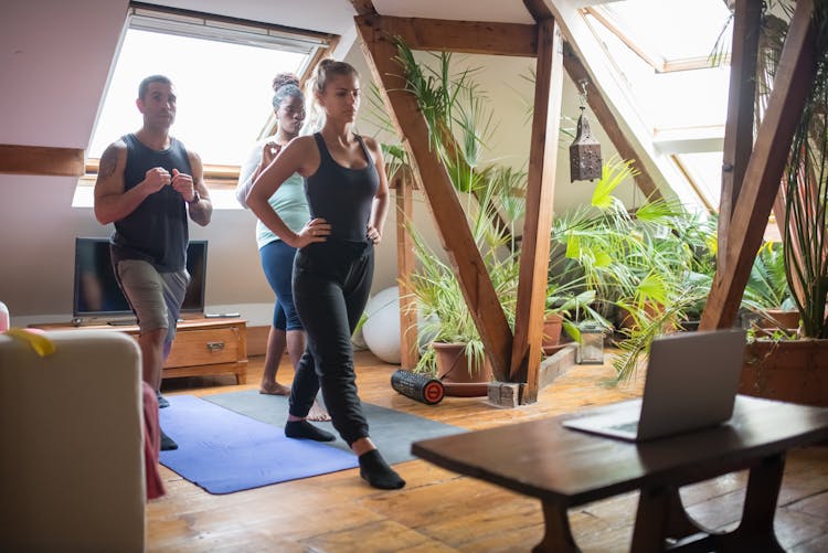 Fitness Group Exercising In The Attic Apartment In Front Of Laptop