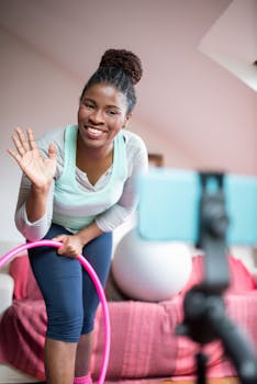 A cheerful woman uses a hula hoop while recording a fitness video indoors.