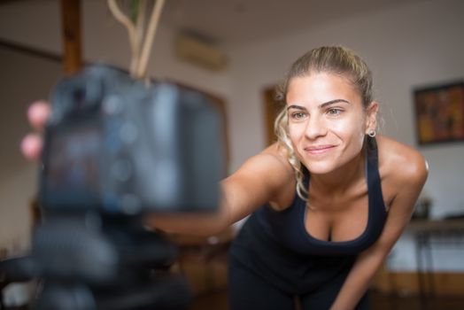 Smiling woman in sportswear setting up a camera indoors for a fitness recording session.
