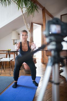 Young woman performing squats indoors in front of a camera, focusing on fitness training.