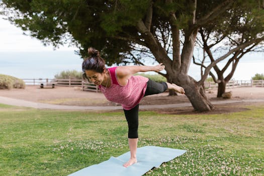 Woman in a balancing yoga pose on a mat in a scenic outdoor park setting.