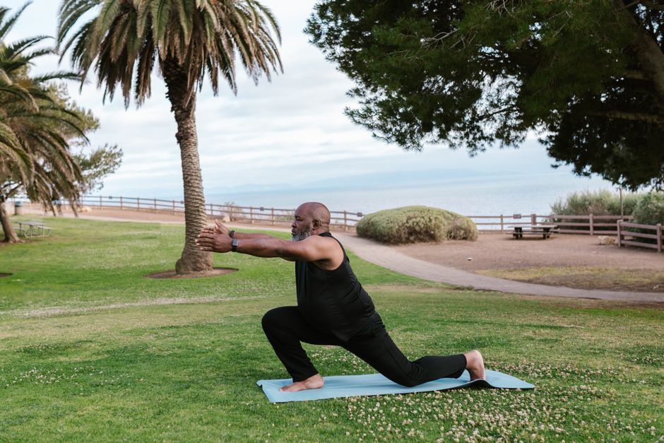 Senior man practicing yoga outdoors on a mat in a park, surrounded by trees and greenery.