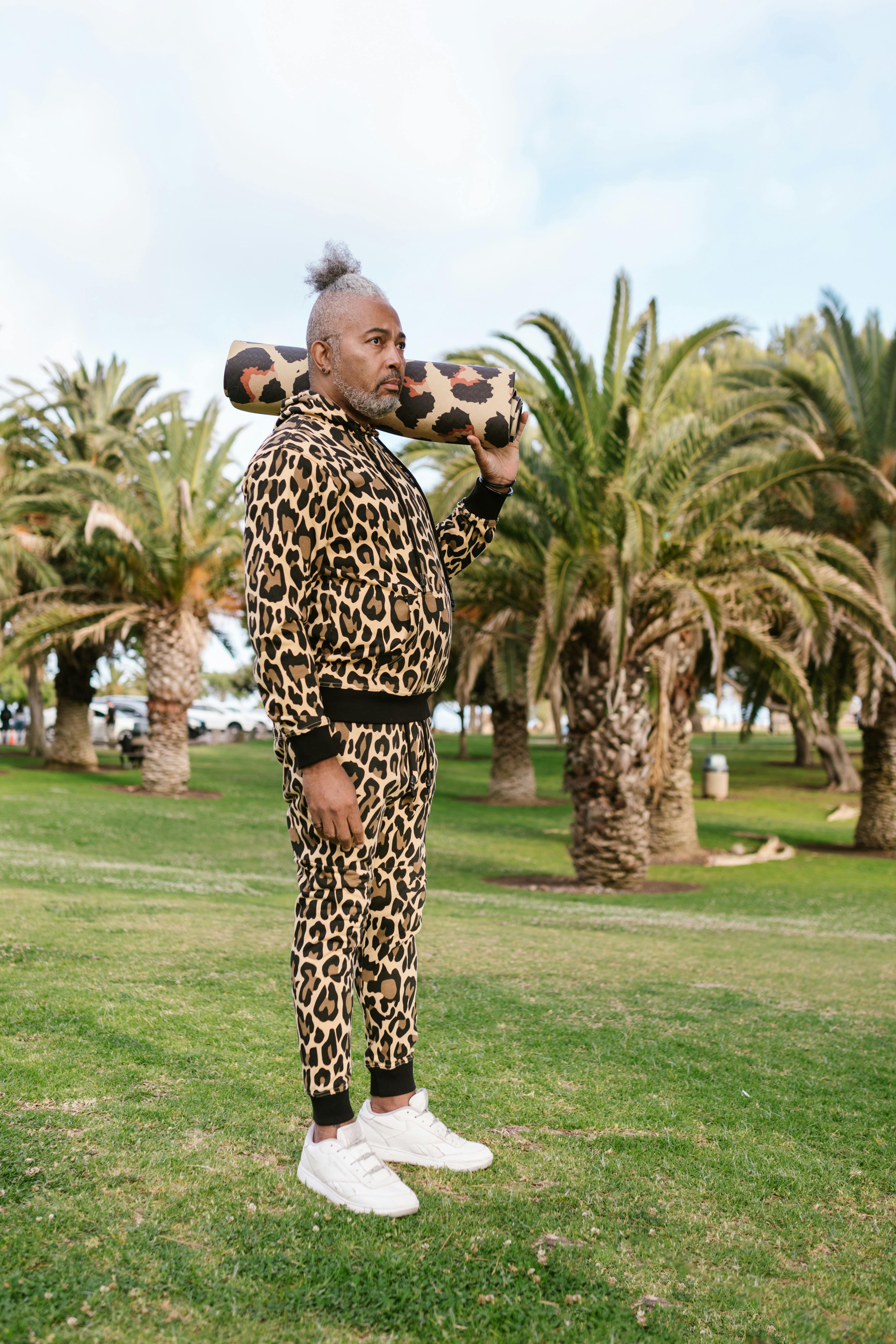 African American man in leopard print stands with yoga mat on shoulder in sunny park.