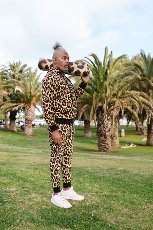 Free African American man in leopard print stands with yoga mat on shoulder in sunny park. Stock Photo