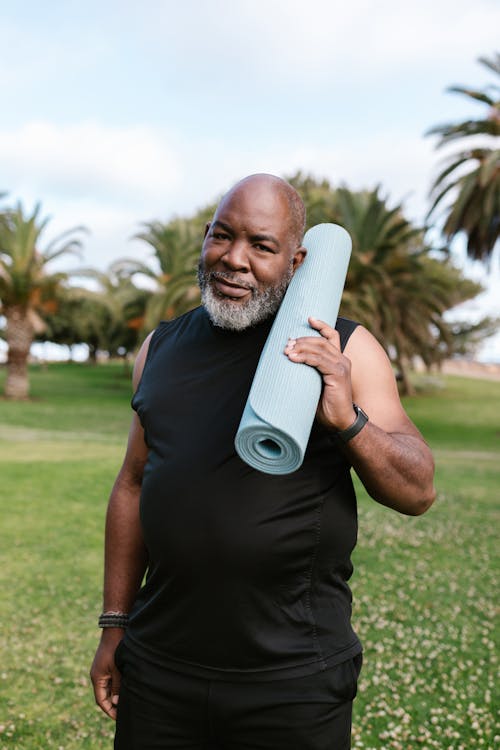 Free An Elderly Man in Black Tank Top Smiling while Holding His Yoga Mat Stock Photo
