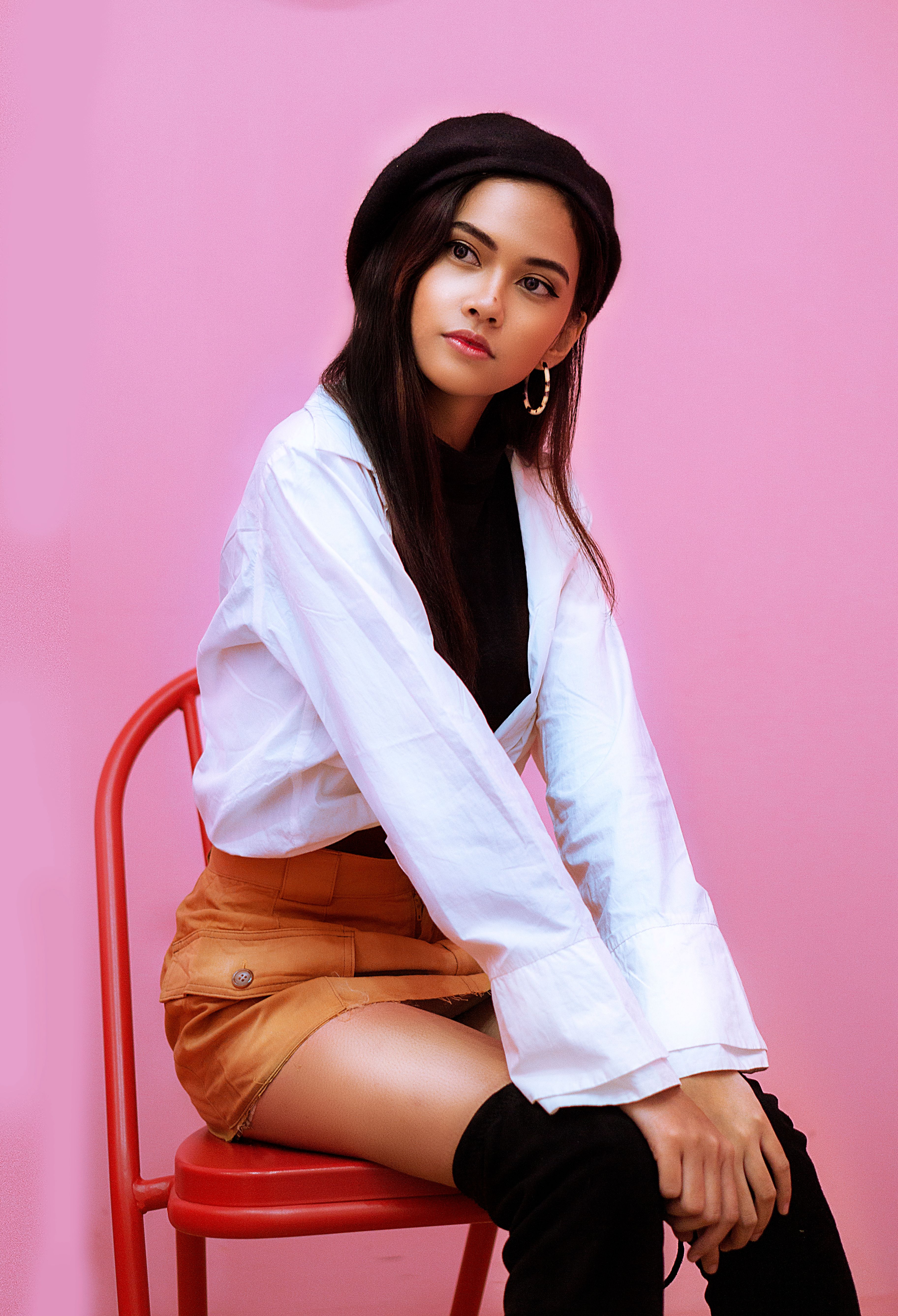 Chic portrait of a woman in a stylish outfit sitting on a chair against a pink backdrop.